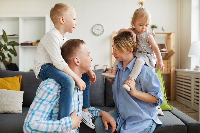 Happy young parents riding children on necks while playing with them at home, loving parents chatting each other